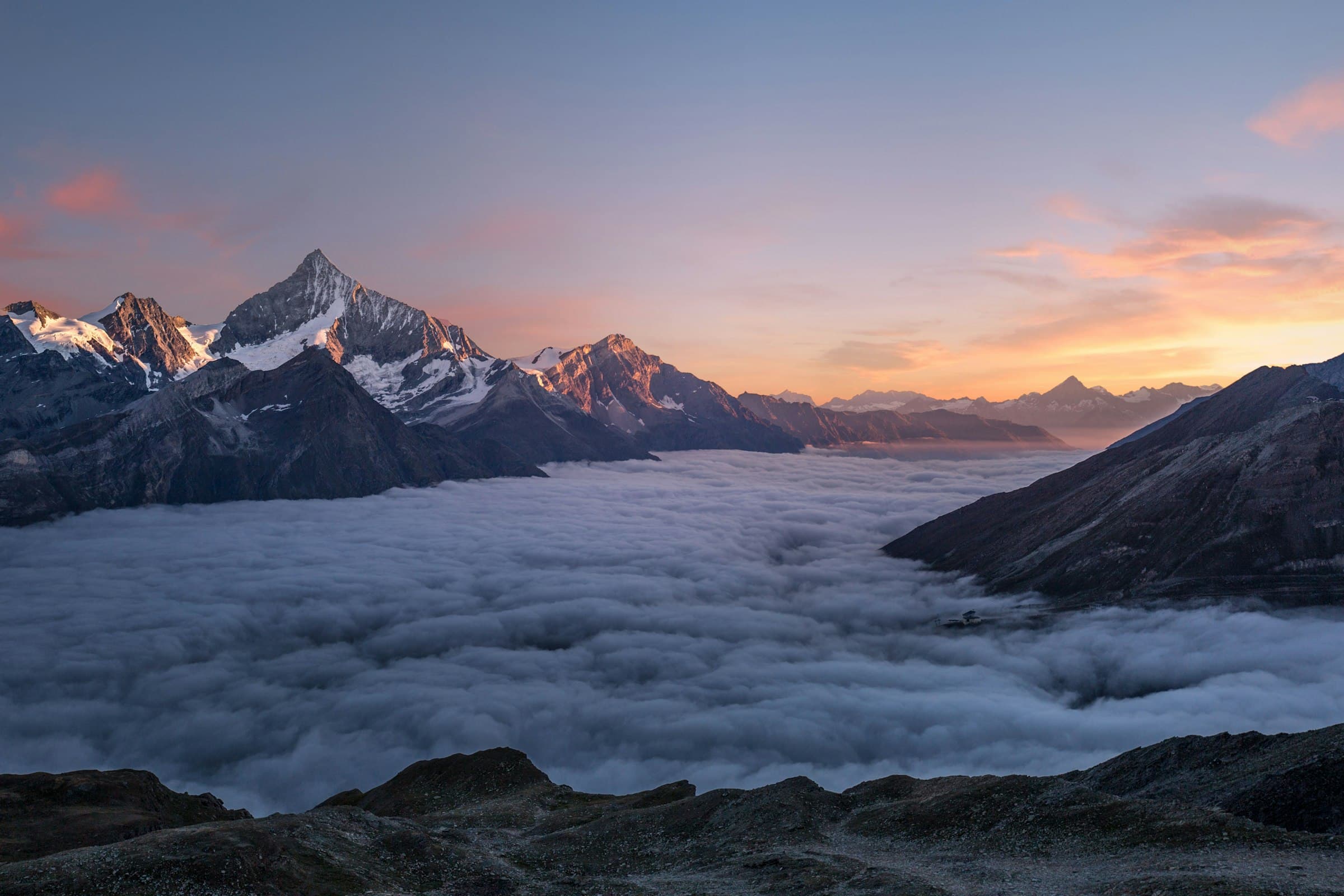 Sunrise on snow-capped Alpine peaks above a valley of cloud