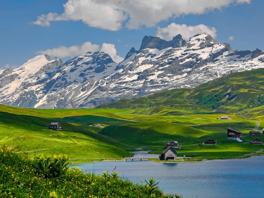 Snow-capped Swiss peaks above green meadows and an alpine lake with chalets